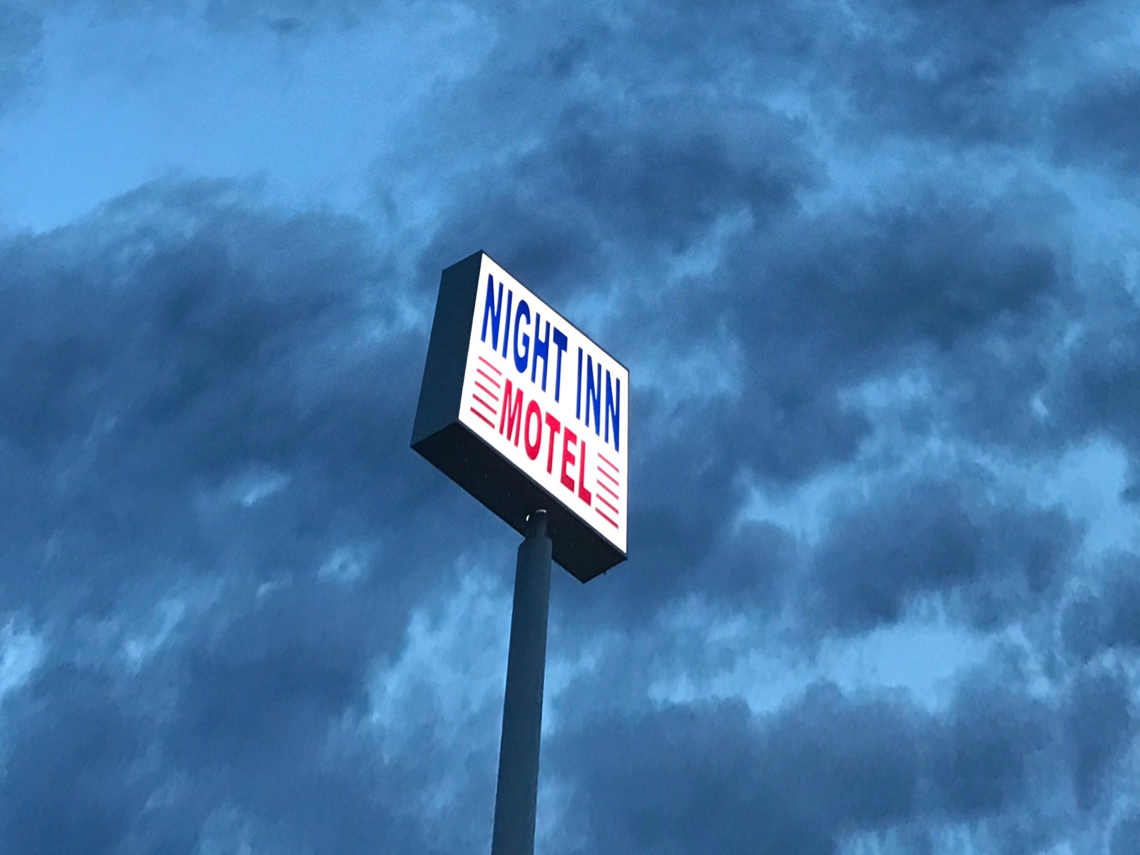 A sign for a motel with the name "NIGHT INN" against a cloudy sky.