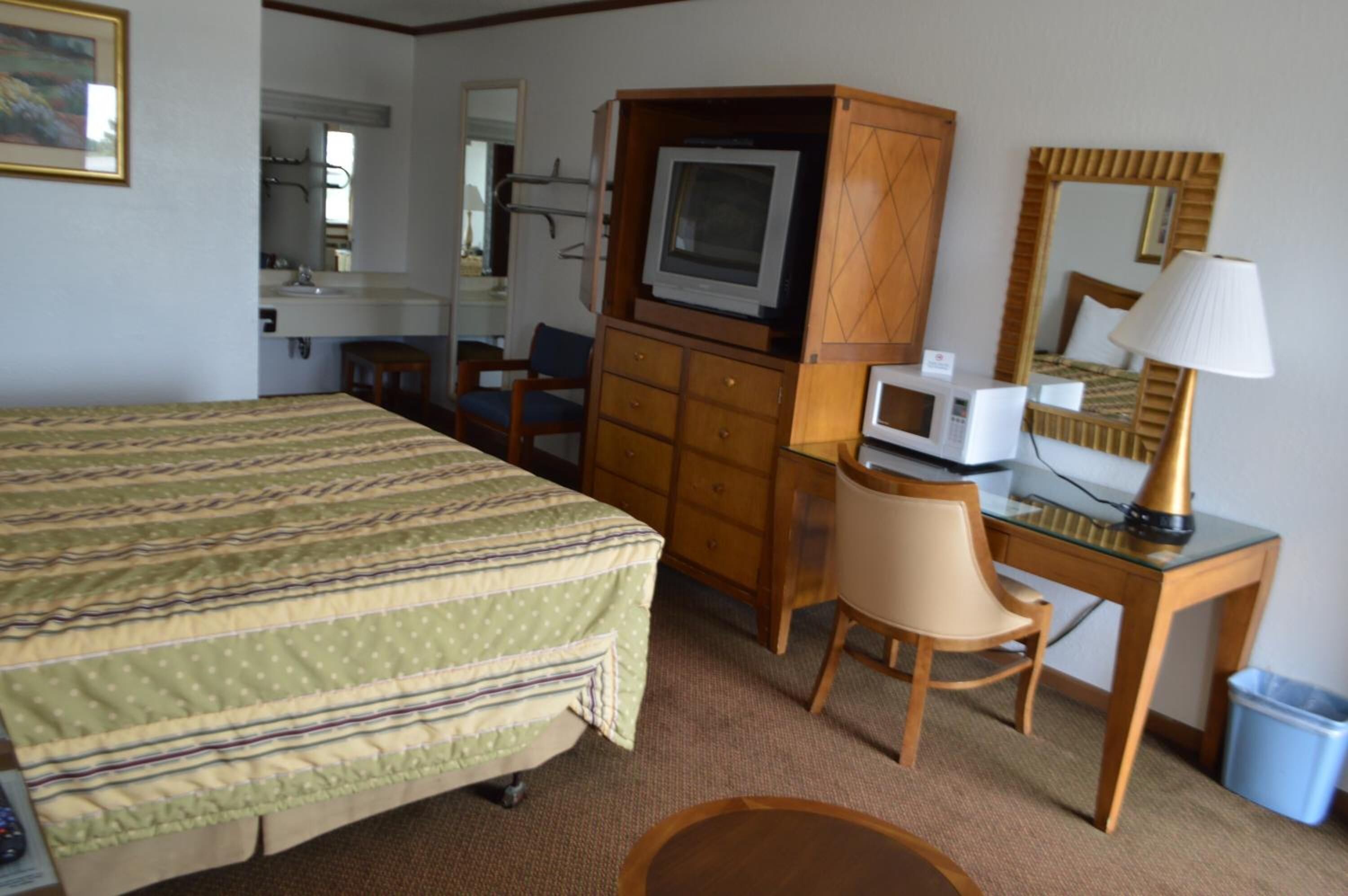 A hotel room with a bed, a desk with a computer, a television, a mirror, and a trash bin.