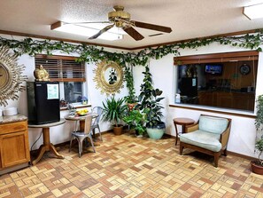 A cozy room with a wooden floor, a ceiling fan, a refrigerator, a dining table with chairs, and various potted plants.