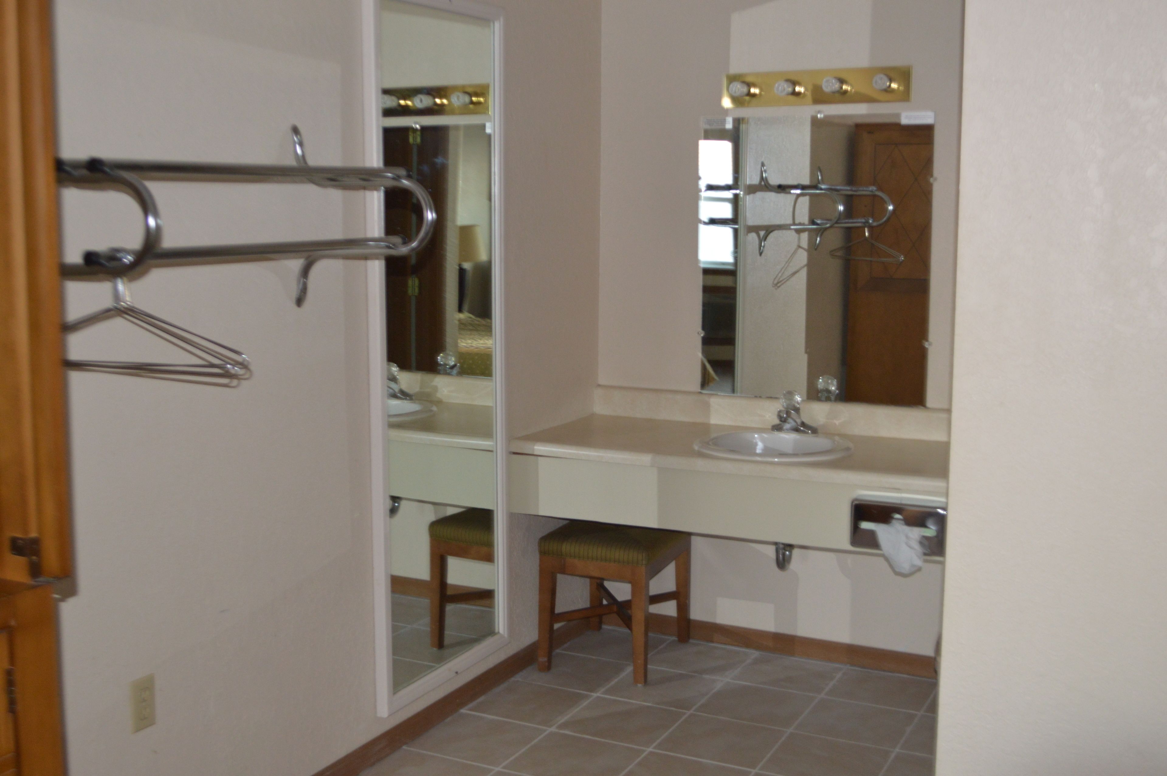 A bathroom with a sink, mirror, towel rack, and a stool.