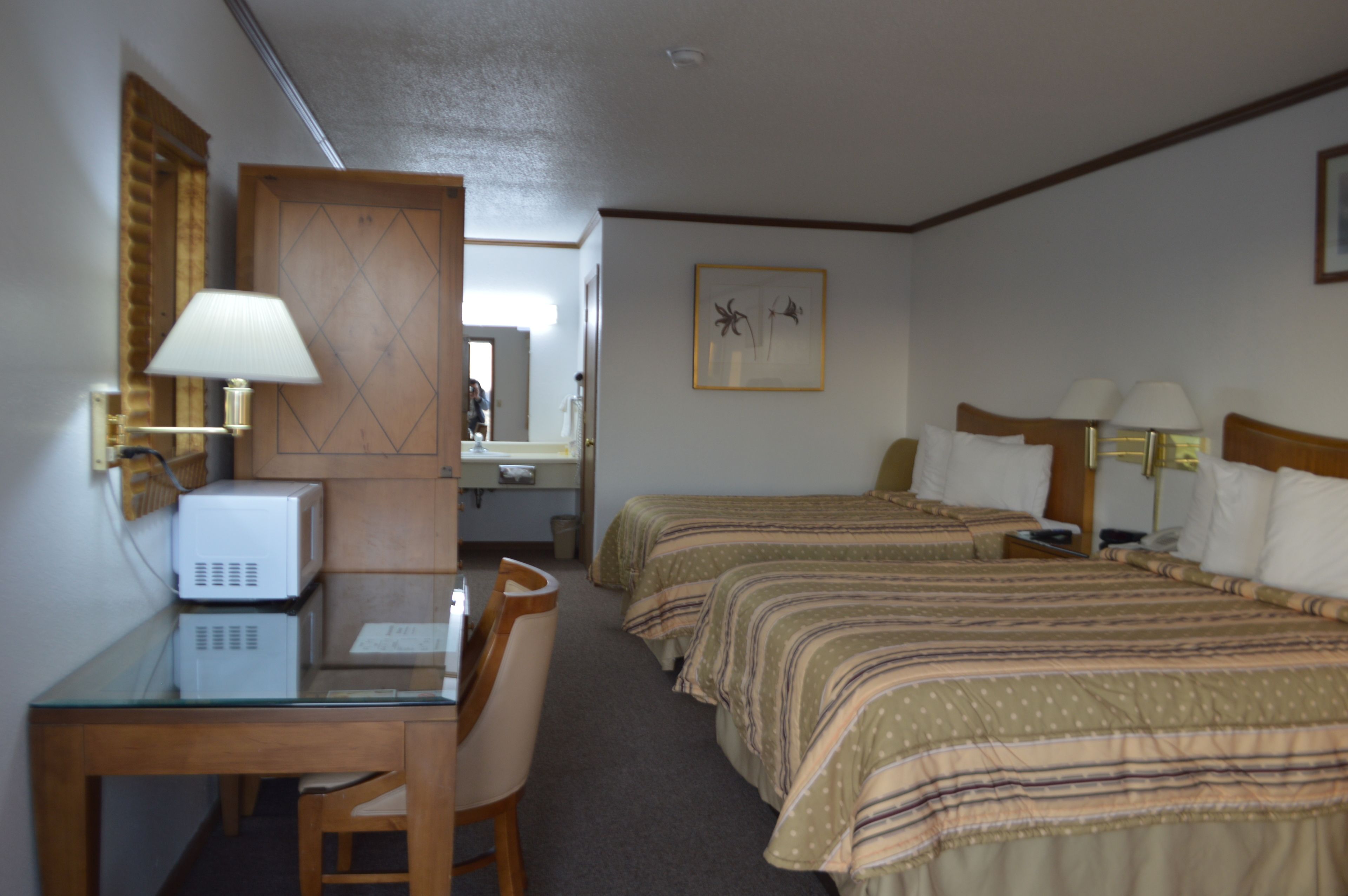 A hotel room with two beds, a desk with a computer, a chair, and a lamp.
