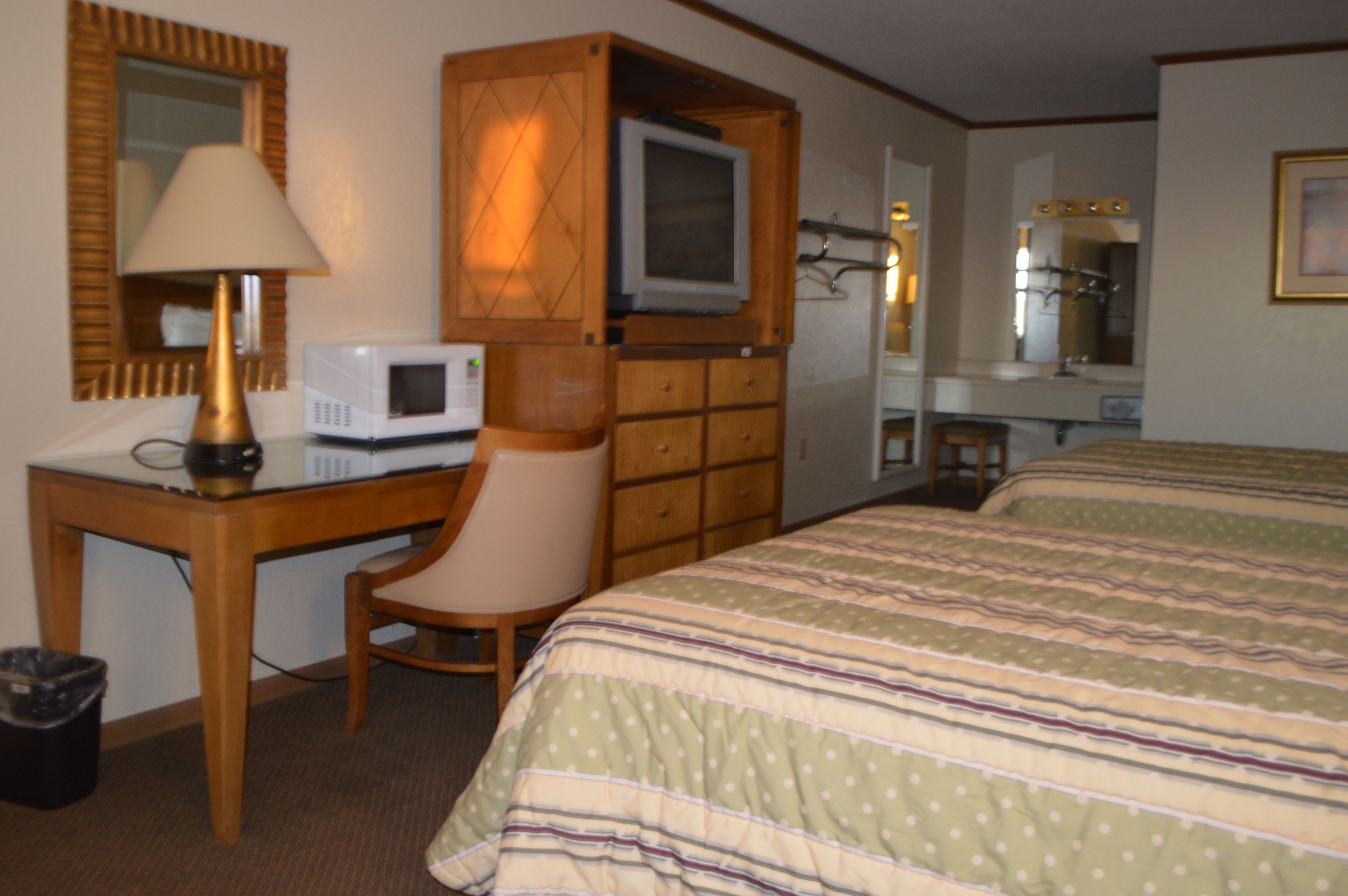 Ein Hotelzimmer mit Holztisch, Fernseher, Sessel, Bett mit gestreifter Bettwäsche, Spiegel und Mülleimer.