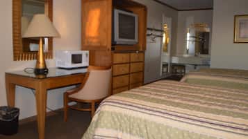 Ein Hotelzimmer mit Holztisch, Fernseher, Sessel, Bett mit gestreifter Bettwäsche, Spiegel und Mülleimer.