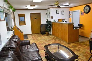 A reception area with a wooden desk, a black leather couch, a glass-top coffee table, and a ceiling fan.