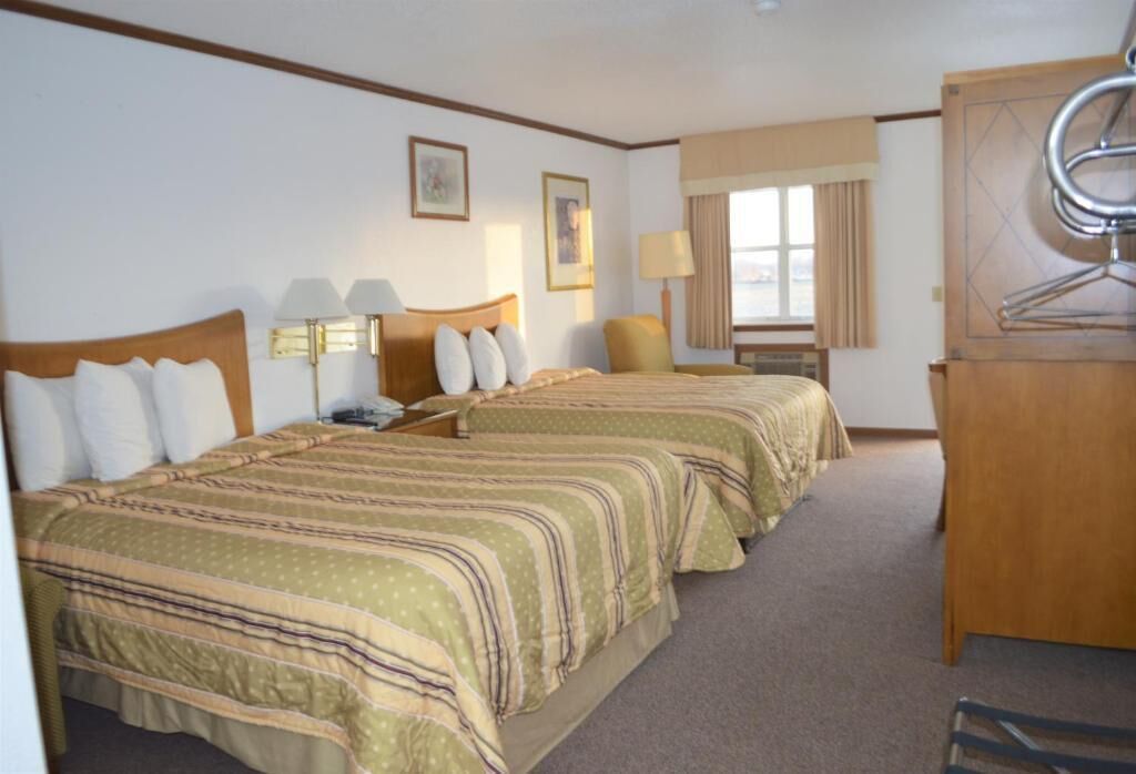 A hotel room with two beds, a desk, a chair, a wardrobe, and a window with curtains.