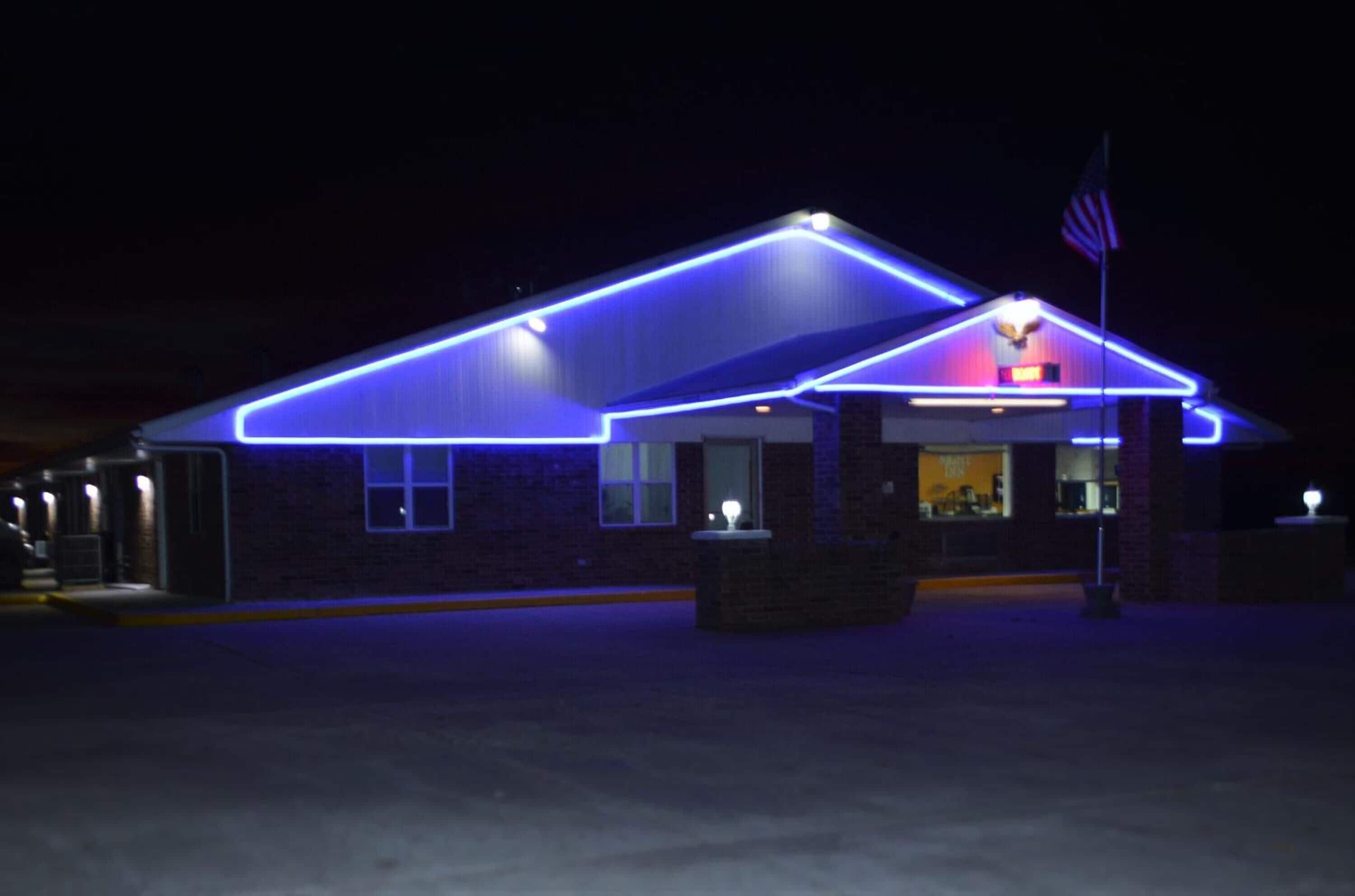 Un edificio con techo plano y fachada de ladrillo, iluminado por luces de neón azules que delinean su estructura.