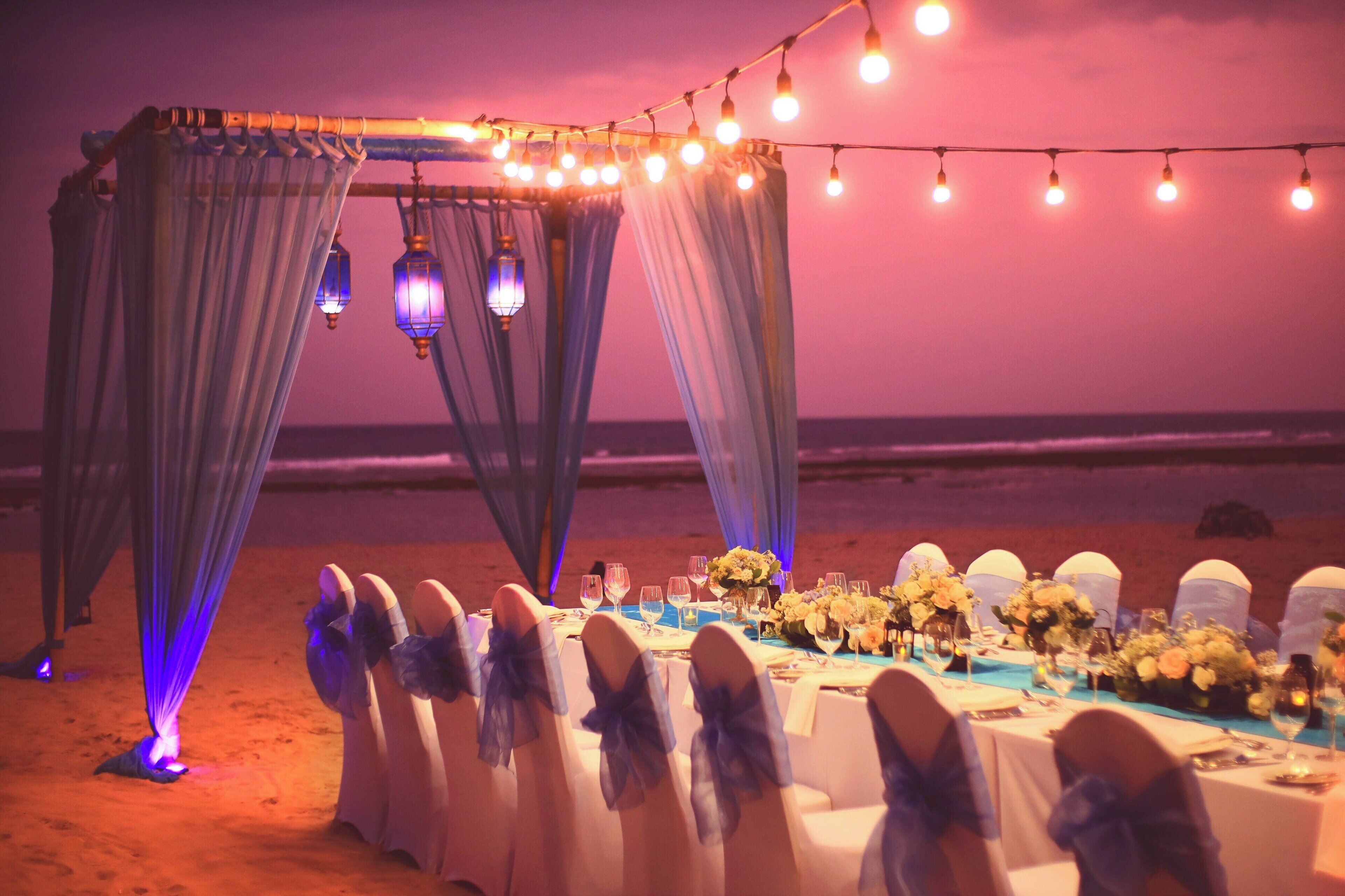 Une cérémonie de mariage organisée sur la plage, avec des tables, des chaises et des guirlandes lumineuses.