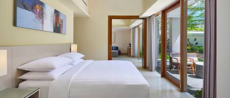A hotel room with a large bed, a bedside table, a painting on the wall, and a view of the outdoor area through a sliding glass door.