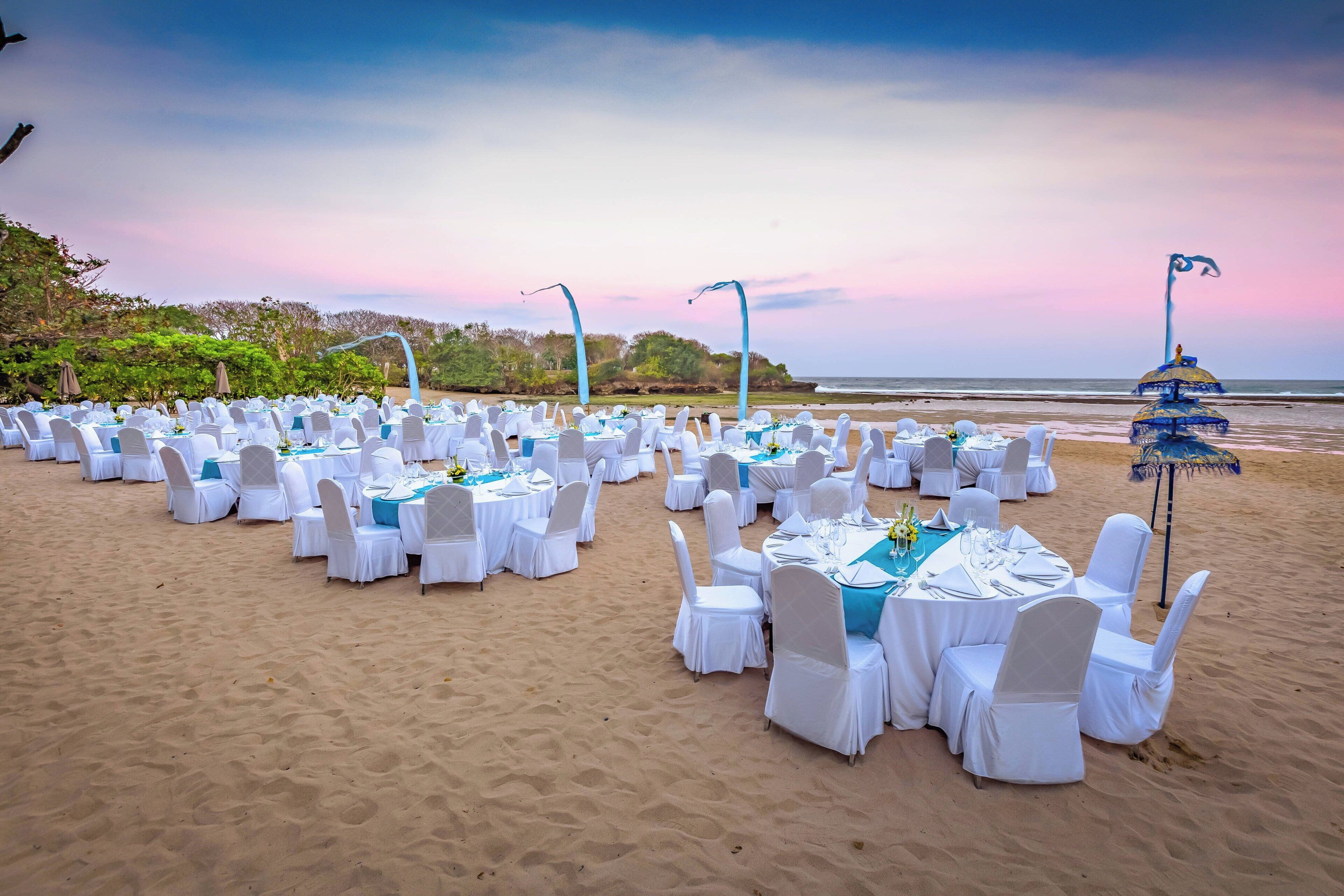 Montaje para un evento en la playa con mesas y sillas redondas, dispuestas en filas, con vista al océano.