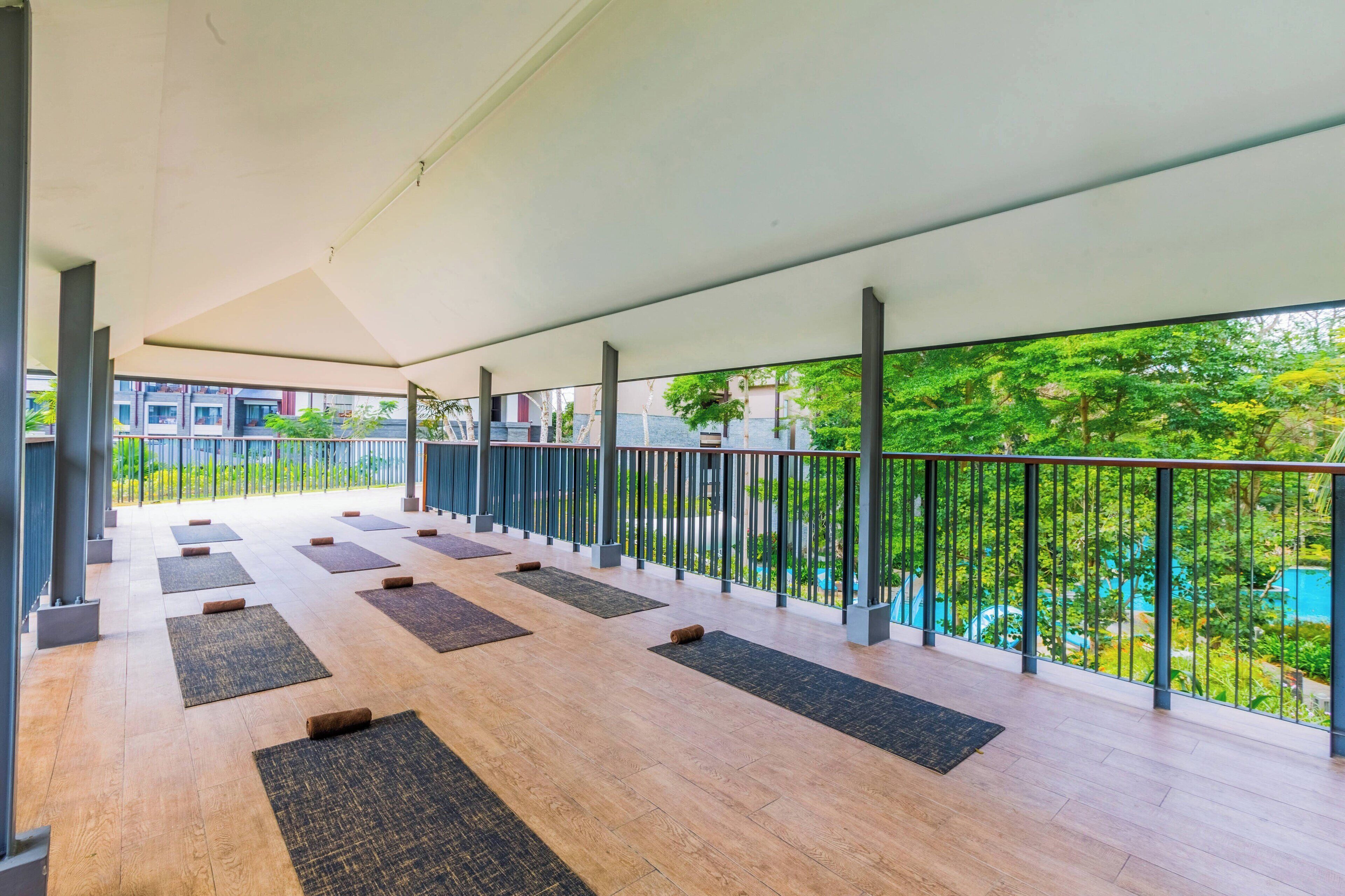 A spacious balcony with wooden flooring, black mats, and a metal railing.