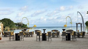 A beachside restaurant with outdoor seating, a view of the ocean, and a curved architectural feature. - Courtyard by Marriott Bali Nusa Dua Resort (Nusa Dua)