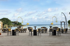 A beachside restaurant with outdoor seating, a view of the ocean, and a curved architectural feature.