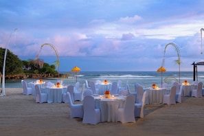 A beachside dining setup with round tables, white chairs, and umbrellas.