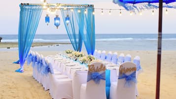 A beach wedding setup with a table adorned with white tablecloths and chairs with 'Bride' and 'Groom' signs.