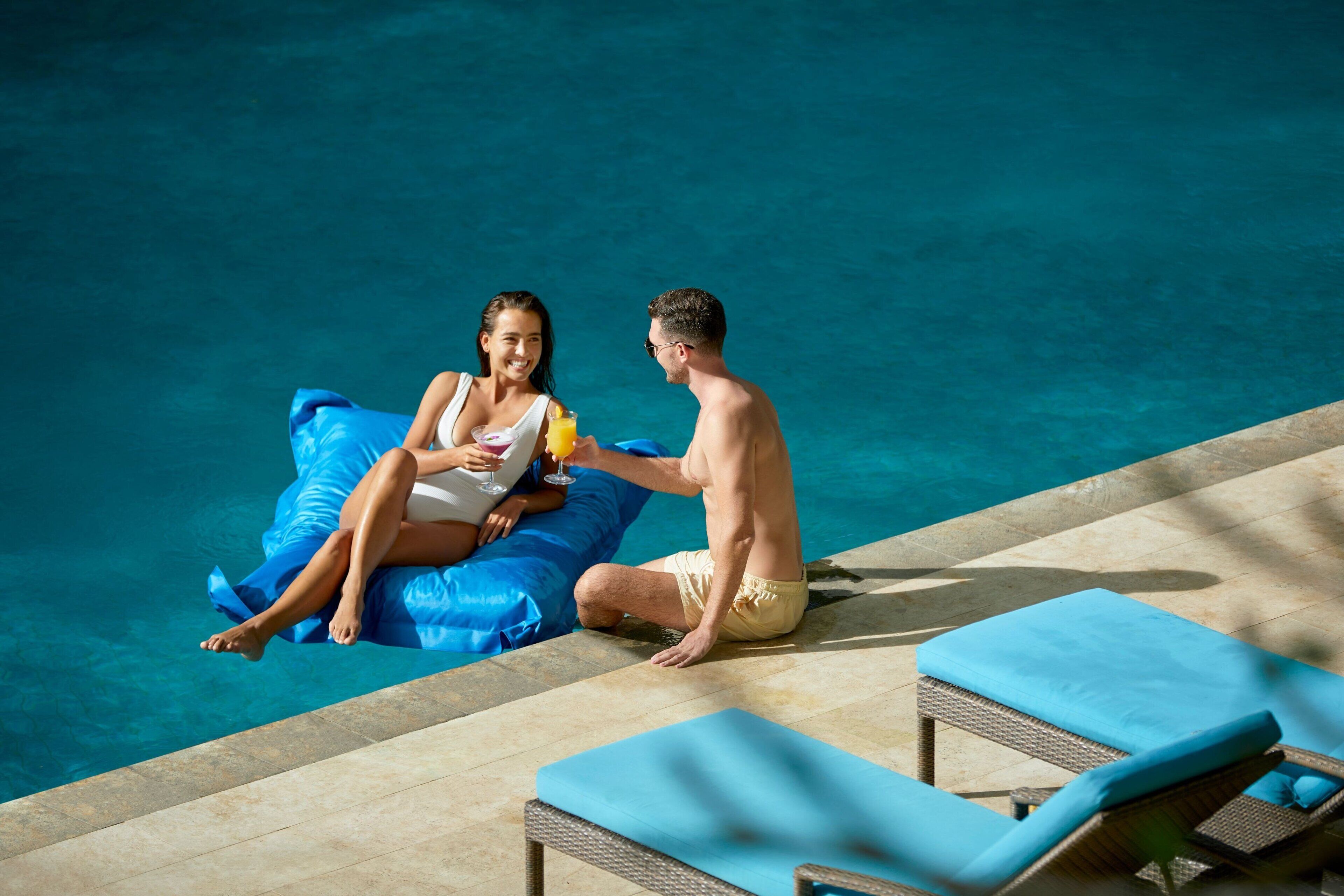 Zona de piscina con sillones de descanso y una persona sentada en un flotador inflable.