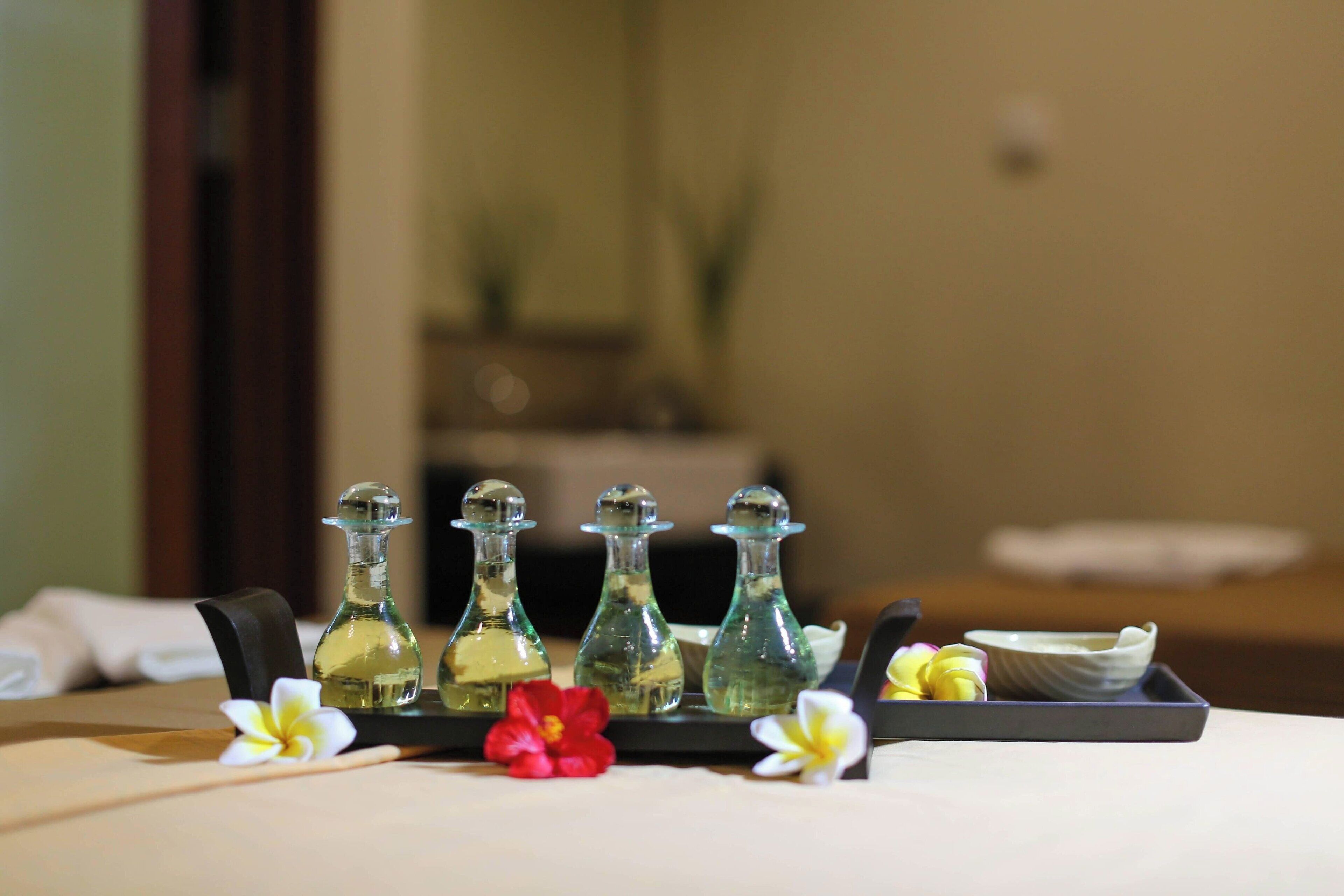 A tray with four glass bottles, a bowl, and two flowers on a table.
