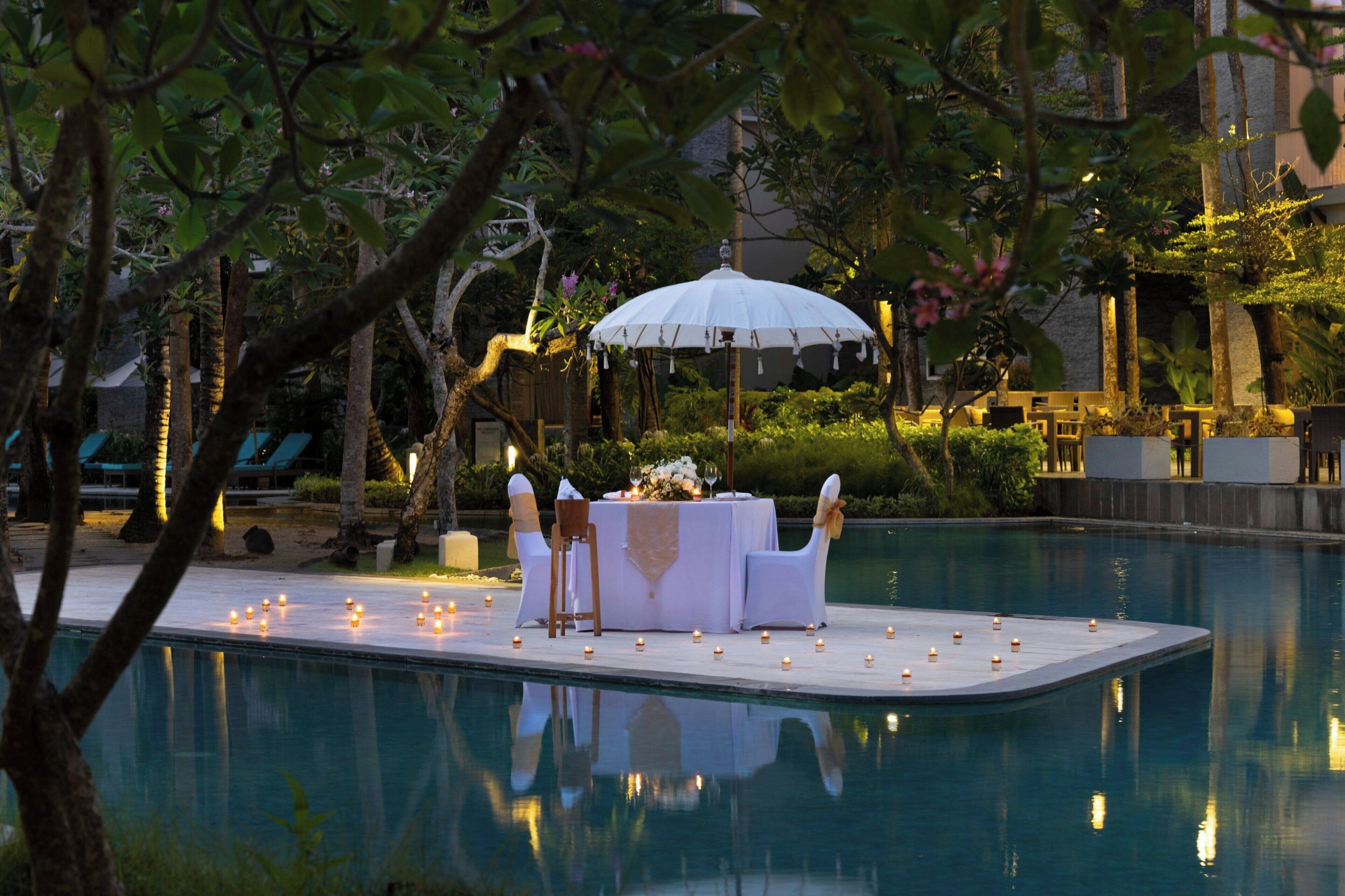 A poolside setting with a table and chairs, candles, and an umbrella.