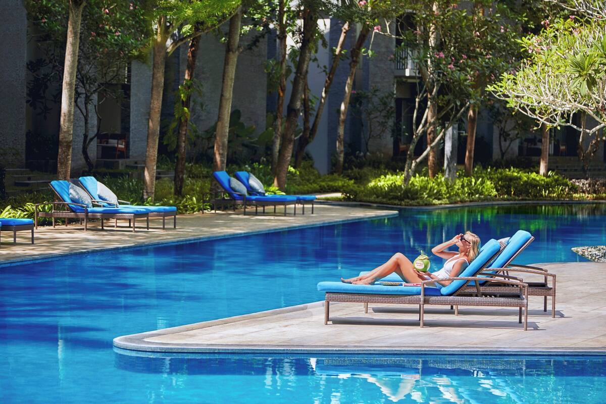A pool area with lounge chairs and a person relaxing by the pool.