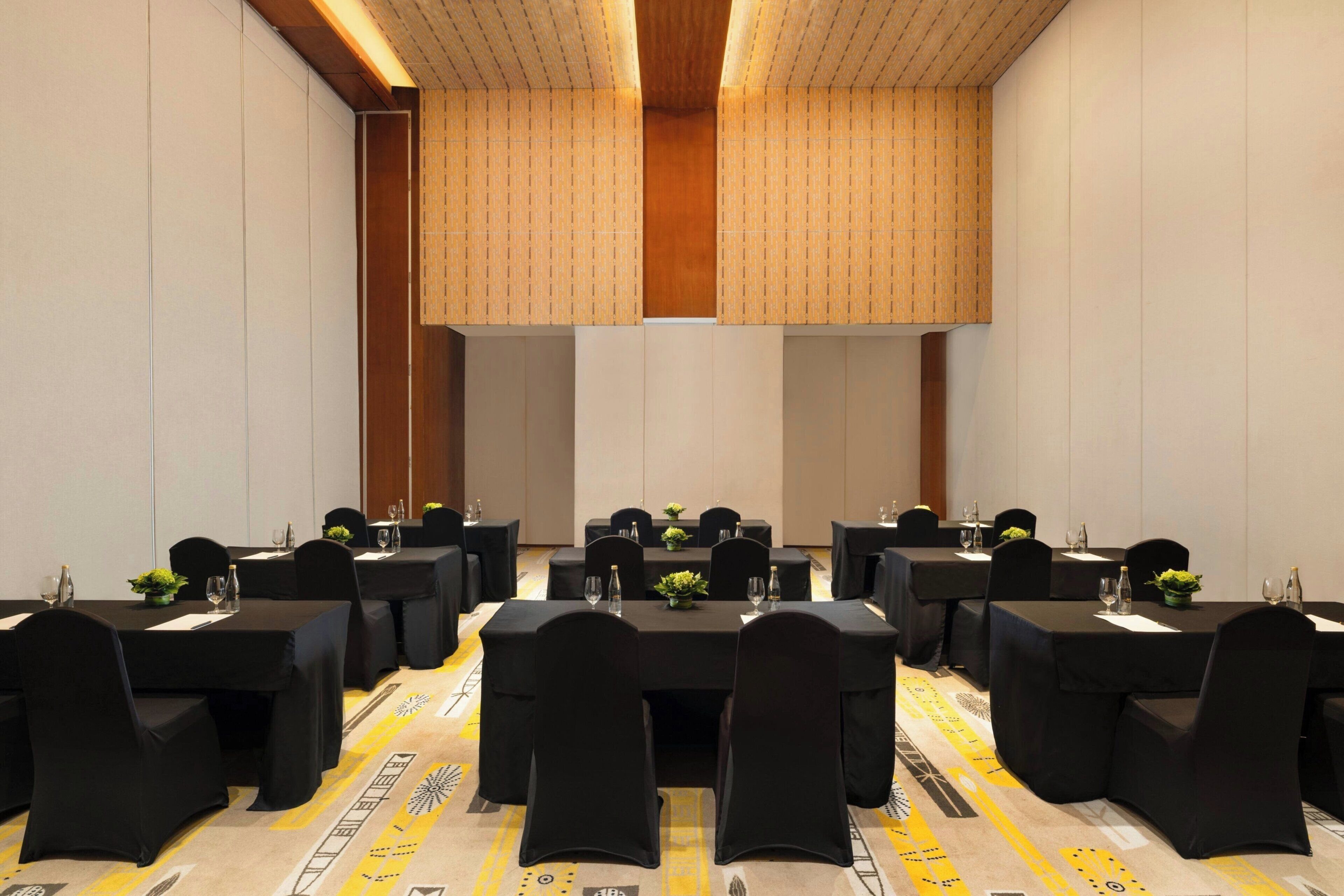 A conference room with multiple tables, black chairs, and a patterned carpet.