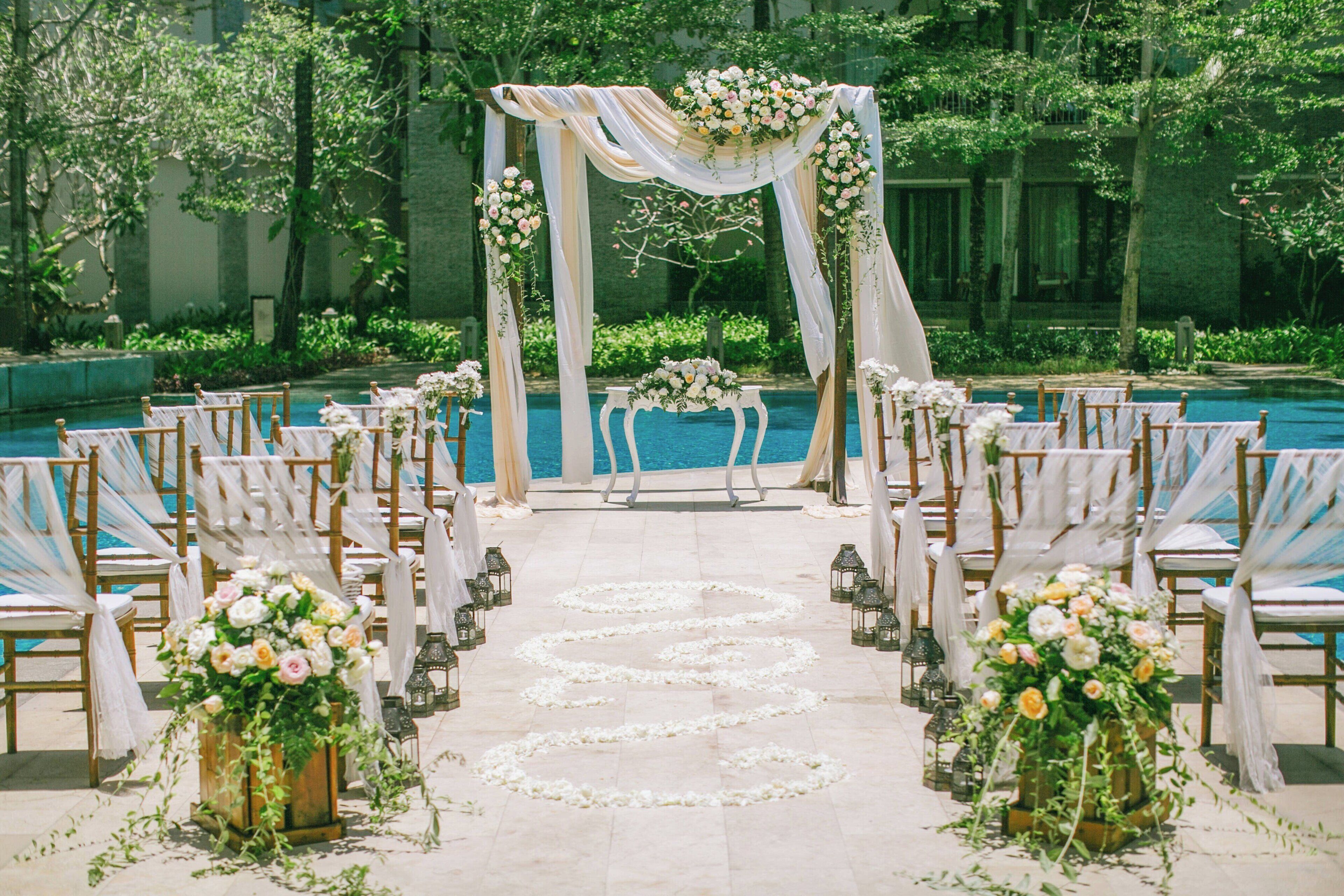 A wedding ceremony setup with a pool, floral decorations, and chairs arranged for guests.