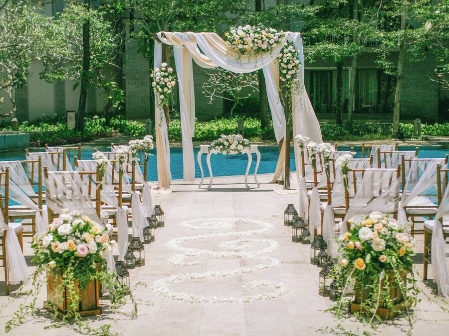Montaje para una ceremonia de boda con piscina, decoración floral y sillas dispuestas para los invitados.