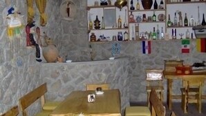 Habitació de pareds de pedra amb una taula i cadires de fusta, una prestatgeria amb diverses ampolles i un petit objecte decoratiu a la paret.