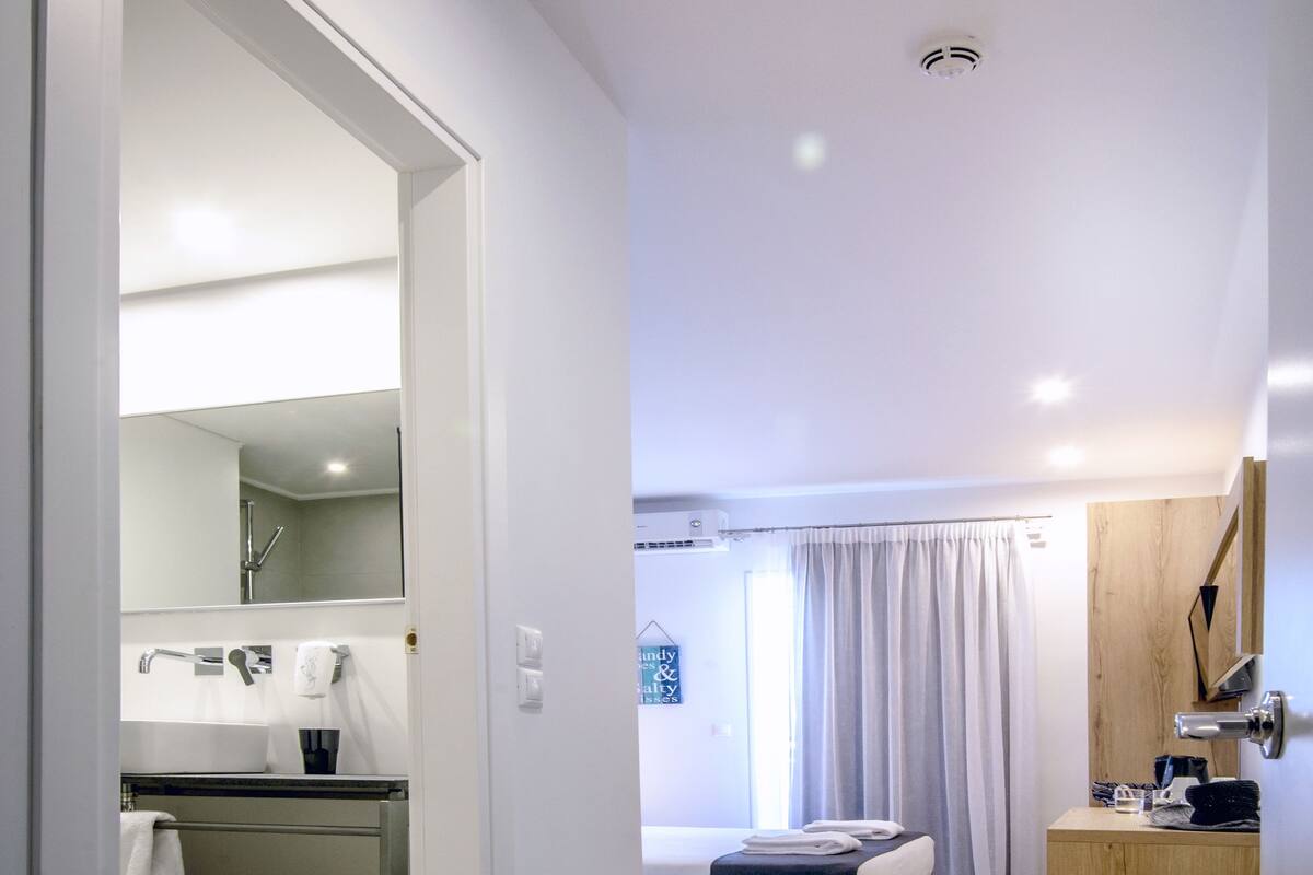 A modern hotel room with a bed, bedside table, and a bathroom with a mirror, sink, and towel rack.
