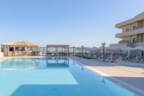 A pool area with lounge chairs and umbrellas, a covered seating area, and a view of the sea. - Zeus Hotels Neptuno Beach - All Inclusive (Malevizi)