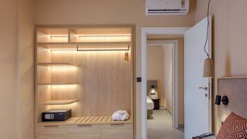 Habitación de hotel con cama, mesita de noche, lámpara y un vestidor con estantes y un banco.