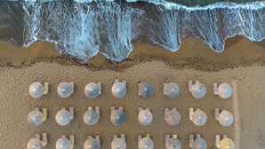 Luftaufnahme eines Strandes mit Reihen von Strandsonnenschirmen und Liegestühlen.