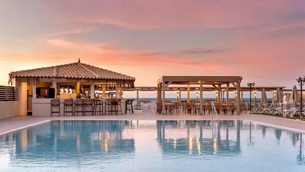 Ein Poolbereich mit Bar und Sitzgelegenheiten mit Blick auf das Meer bei Sonnenuntergang.