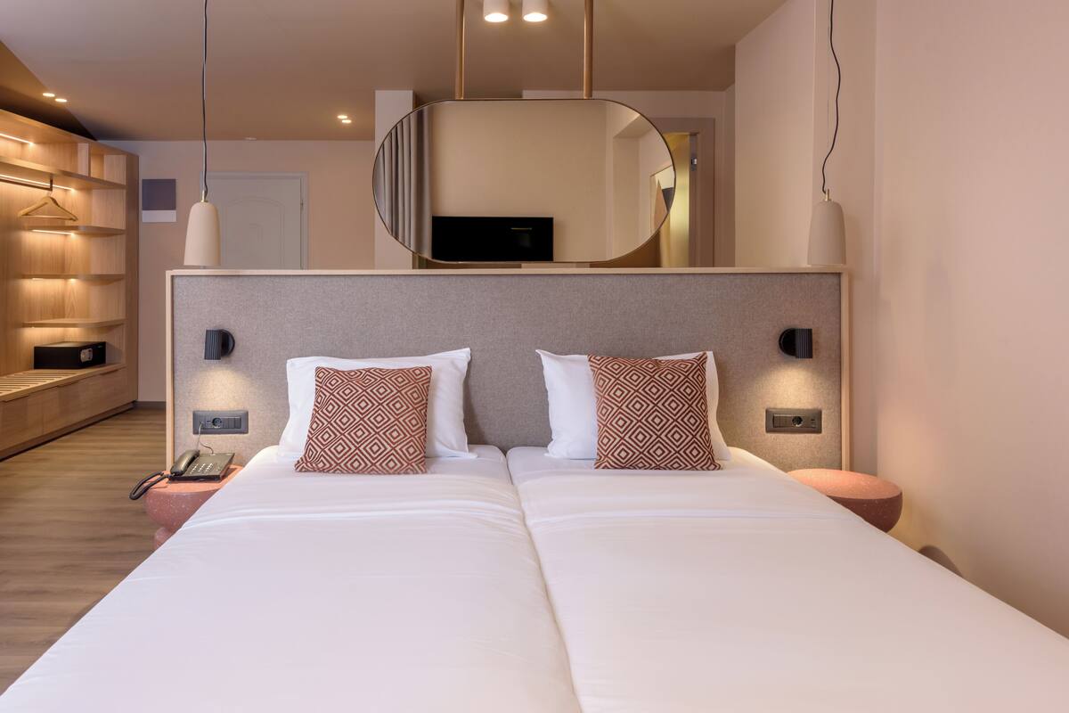A modern hotel room with a large bed, bedside tables, a mirror, and a TV.