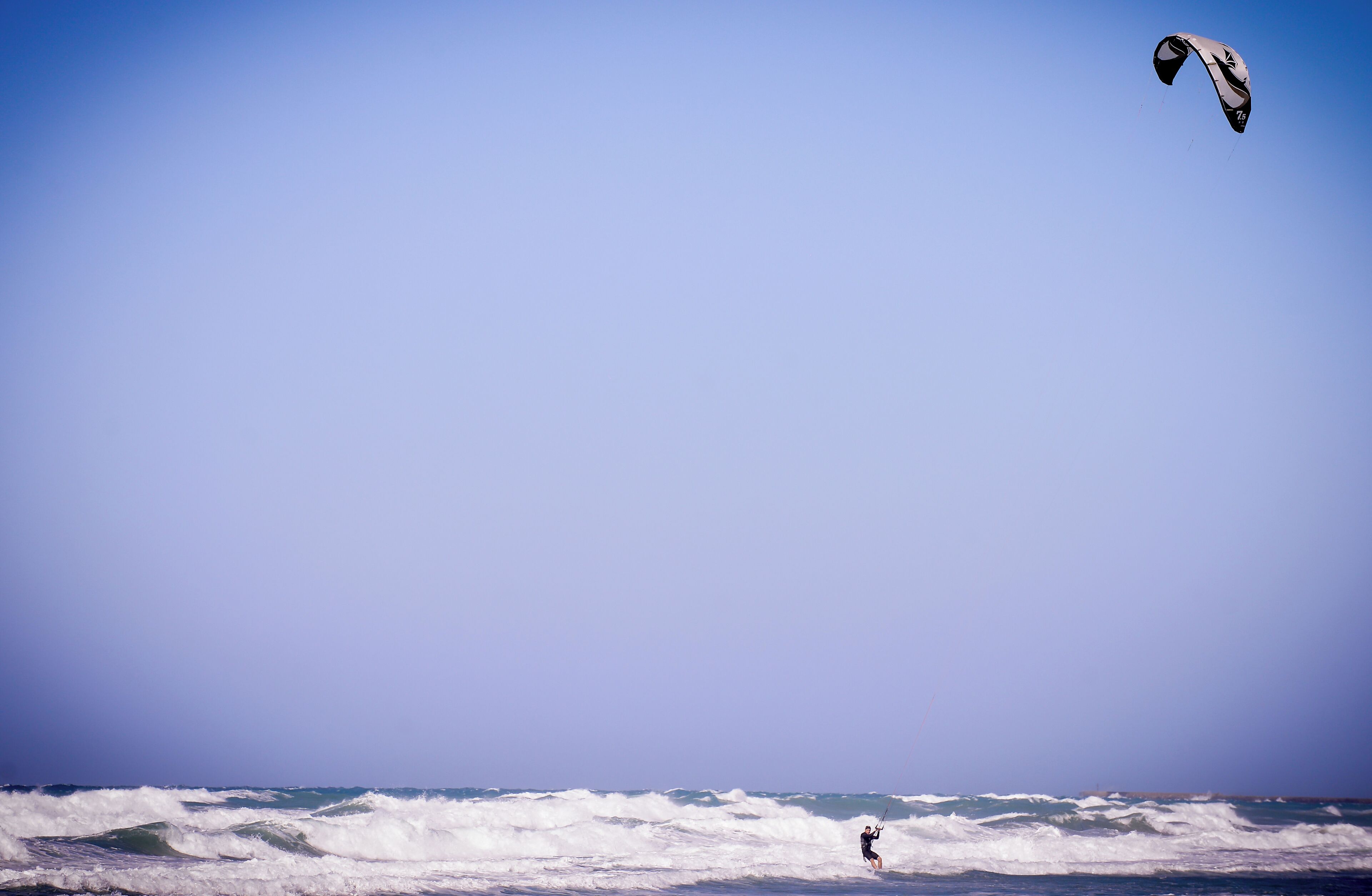 A beach scene with waves and a person windsurfing.