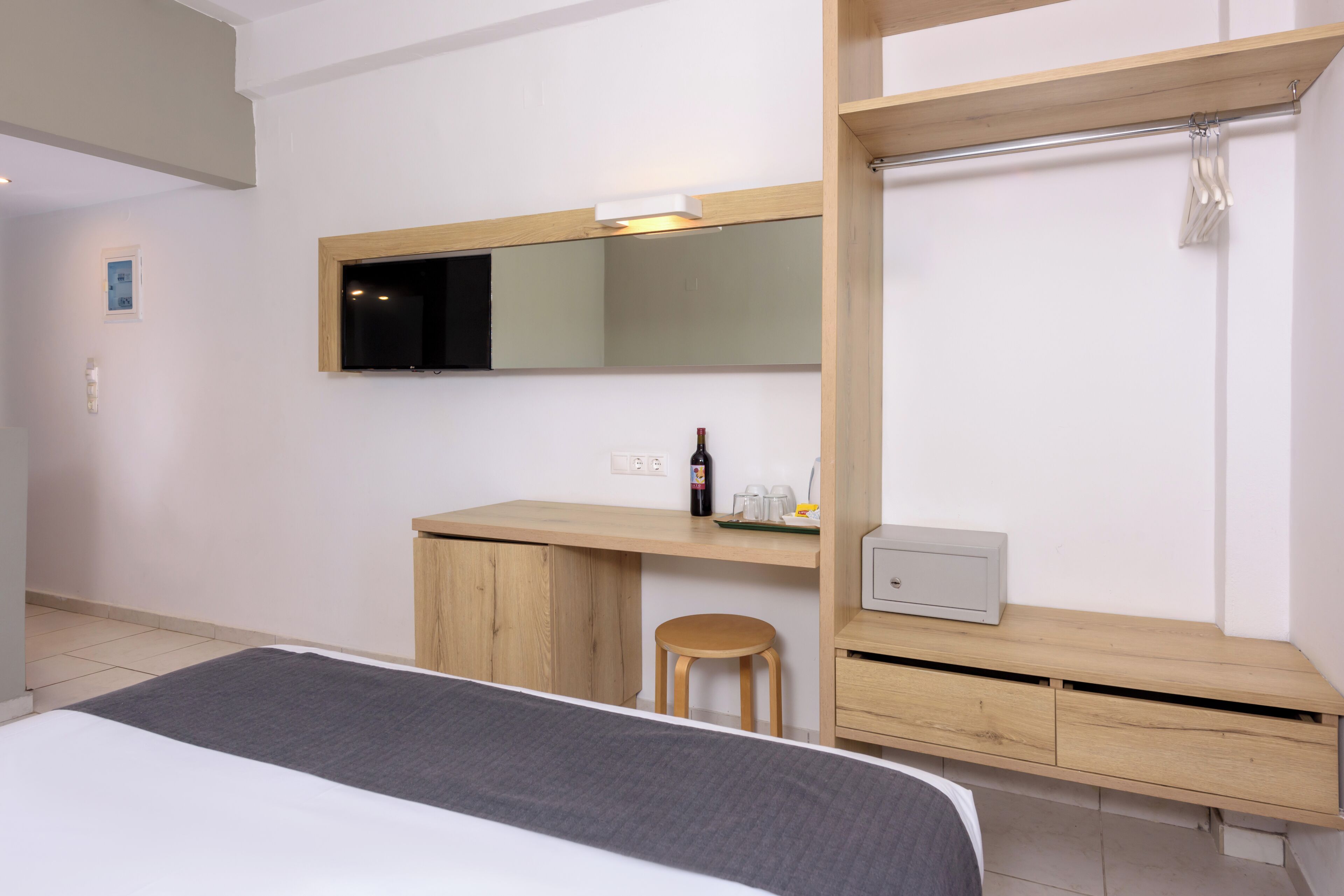 A hotel room with a bed, a desk, a chair, a mirror, and a small cabinet.