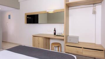 A hotel room with a bed, a desk, a chair, a mirror, and a small cabinet.