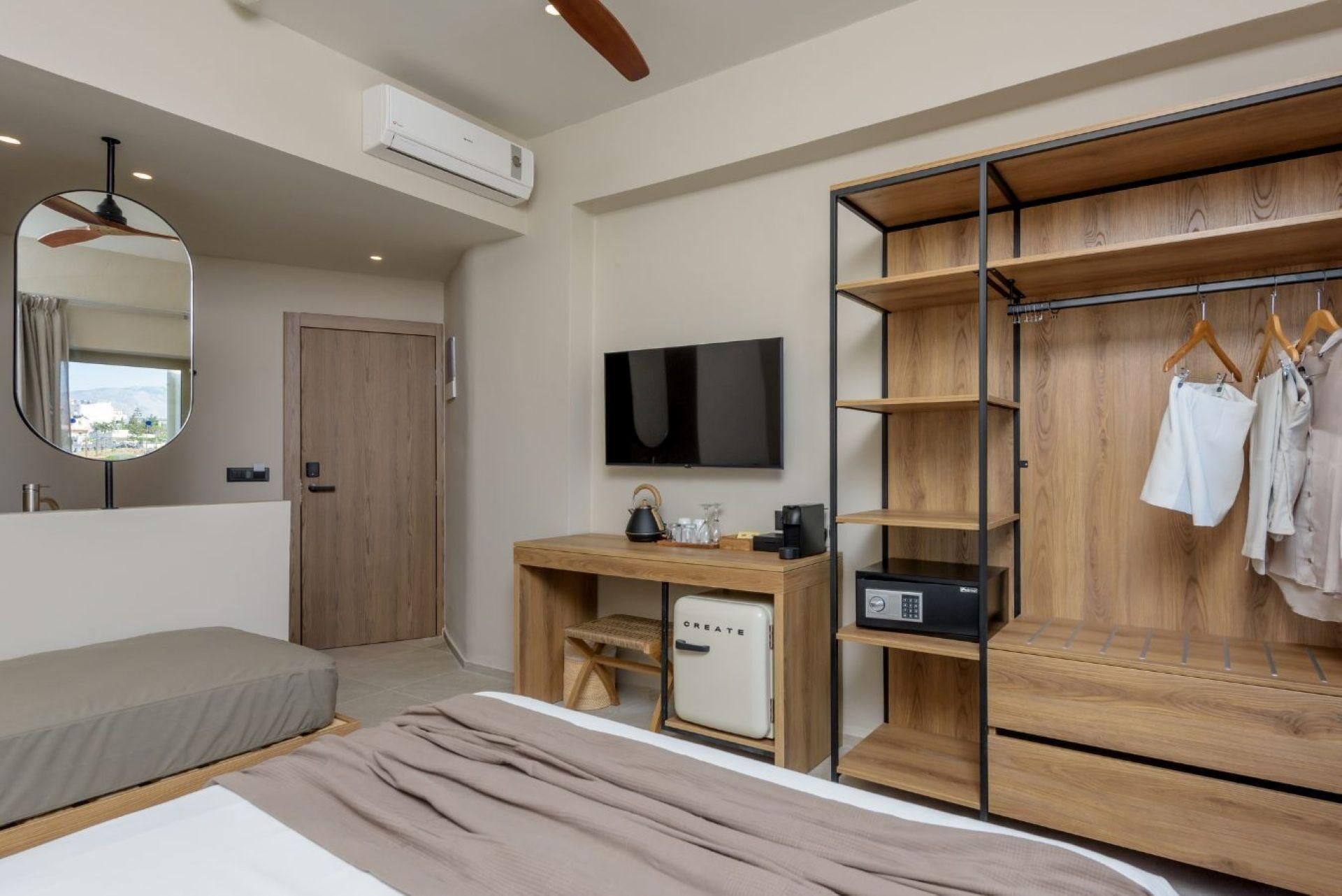 Una habitación de hotel moderna con una cama, un escritorio con computadora, un televisor, un armario y un espejo.