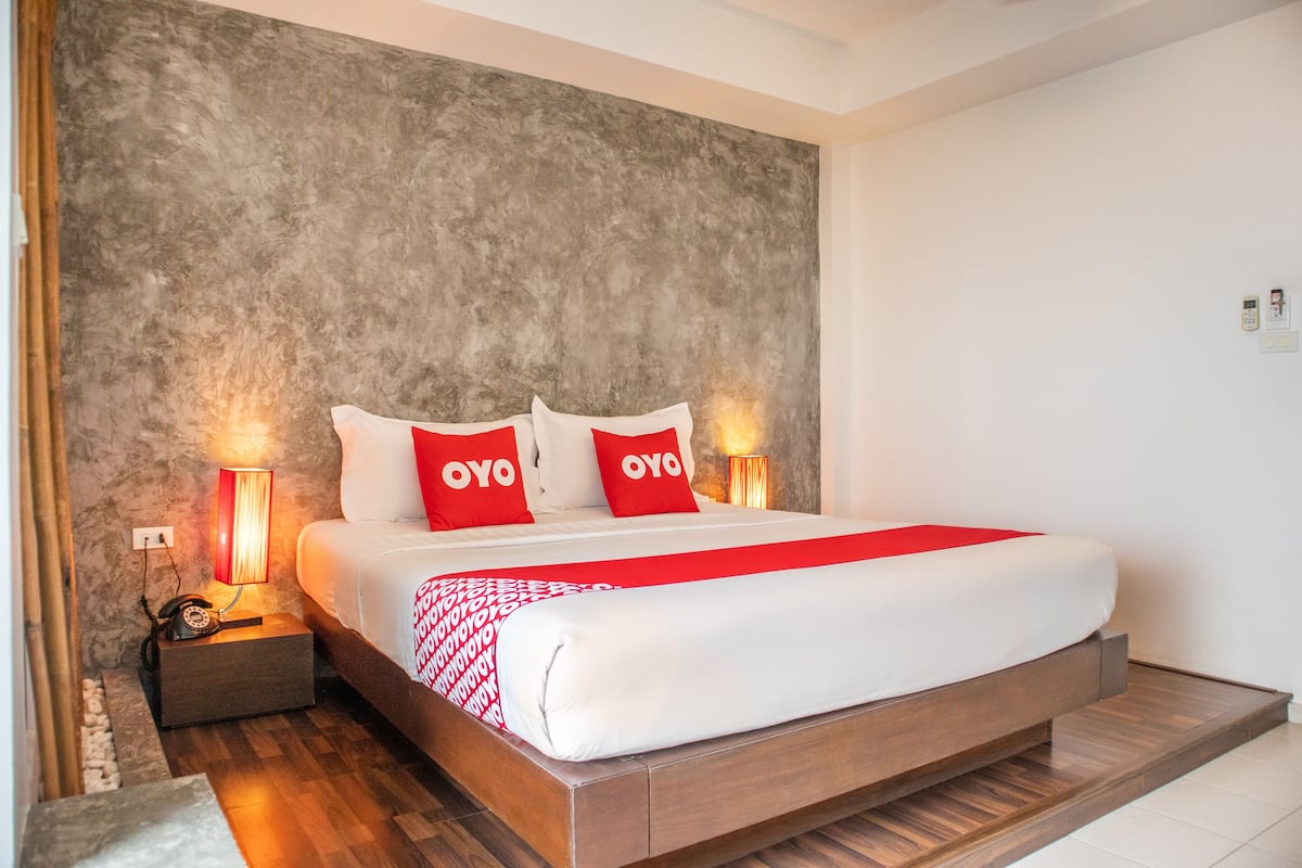 Une chambre d’hôtel moderne avec un grand lit, deux tables de chevet avec des lampes, un mur à motifs et une couvre-lit rouge et blanche.