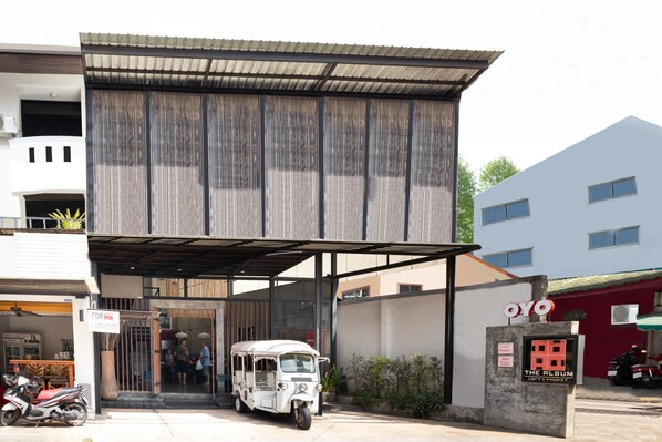 A building with a covered entrance, a sign for a business, and a parked tuk-tuk. - The Album Loft at Nanai (Patong)
