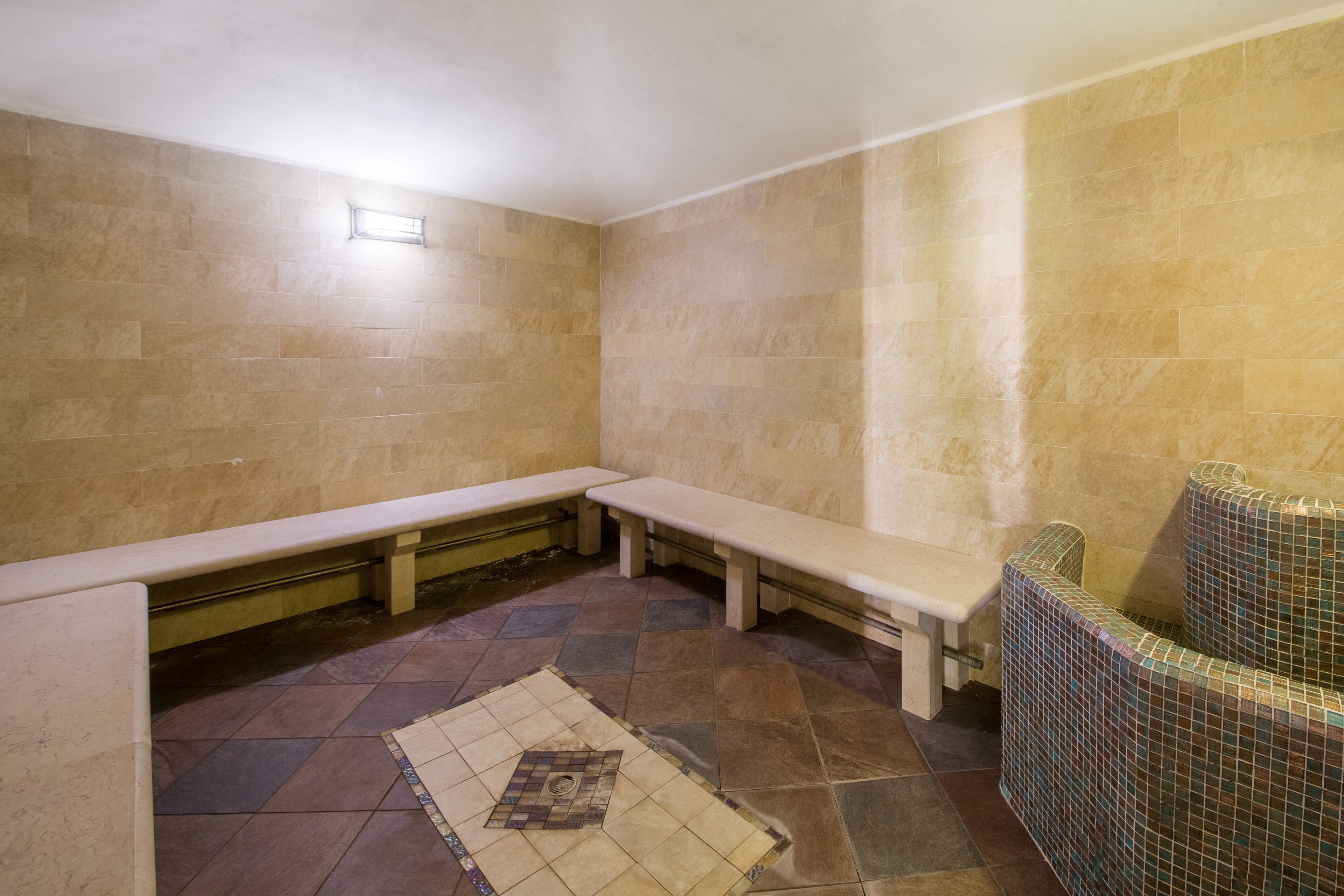 Ein Spa-Raum mit beige gefliesten Wänden, einer Bank, einem gefliesten Boden und einem kleinen Fenster.