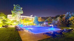 A nighttime swimming pool area with lounge chairs and a building in the background.