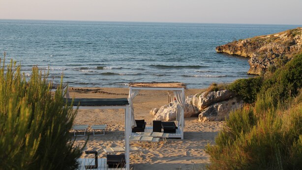 A beach with a wooden gazebo, lounge chairs, and a view of the sea.