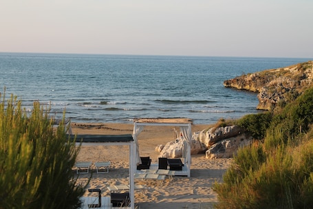 A beach with a wooden gazebo, lounge chairs, and a view of the sea.