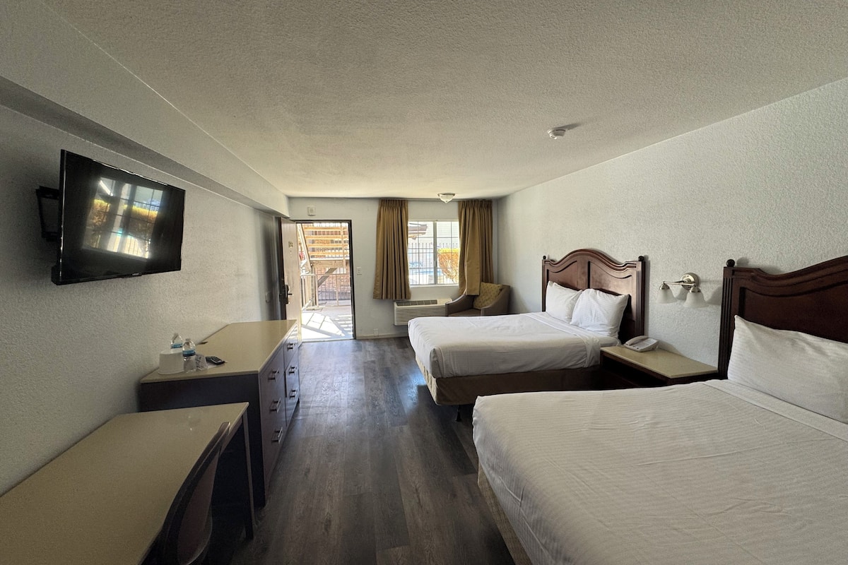 A hotel room with two beds, a TV, a desk, and a window with curtains.