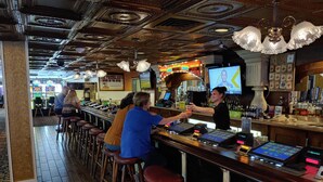 A bar area with wooden floors, bar stools, and a bar counter with a cash register and various bottles. - The New Pioneer (Laughlin)