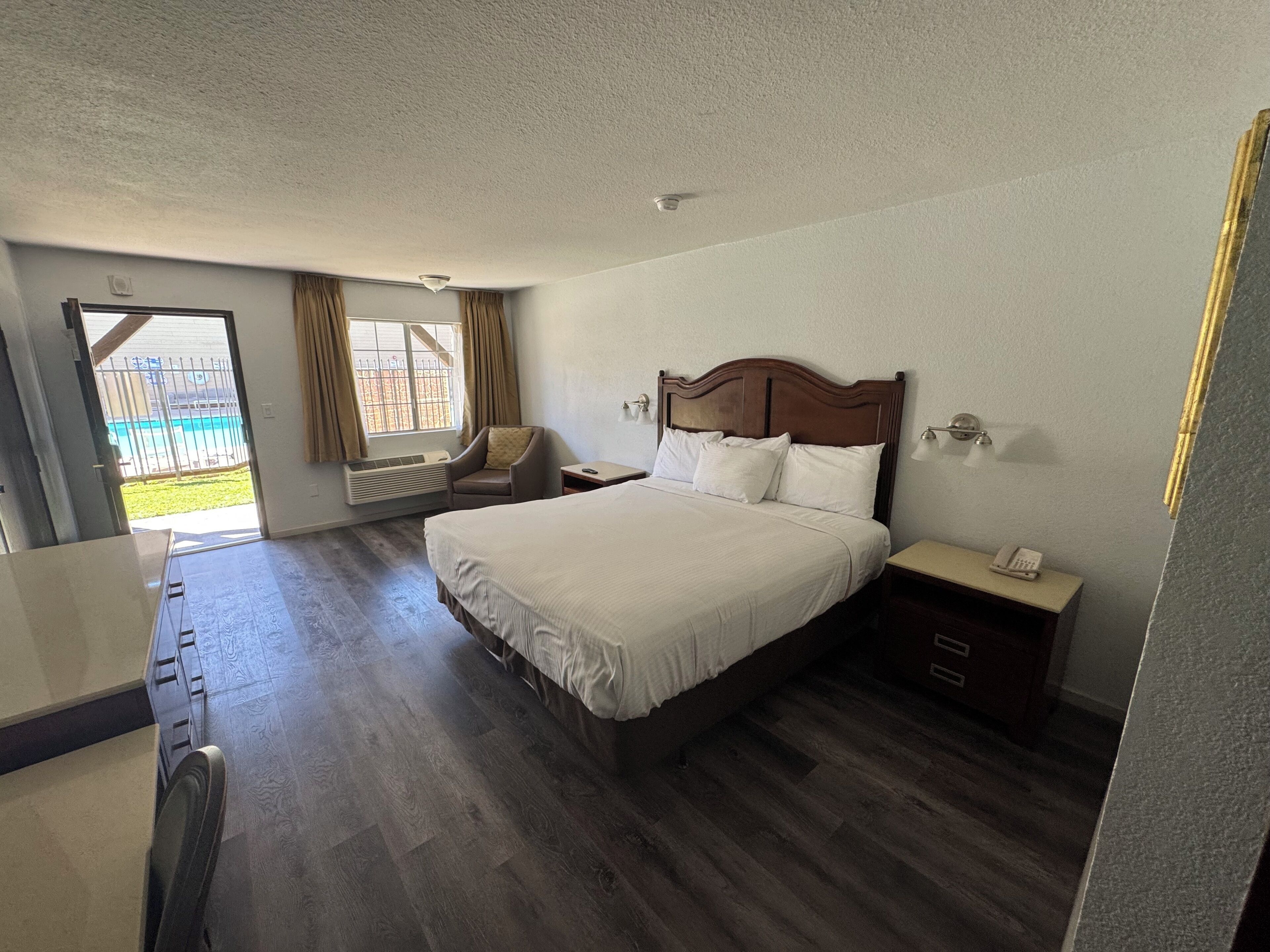 Habitación de hotel con una cama grande, una silla, un escritorio y un ventanal con cortinas.