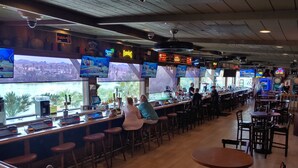 A bar area with multiple screens displaying content, bar counters, and seating arrangements. - The New Pioneer (Laughlin)