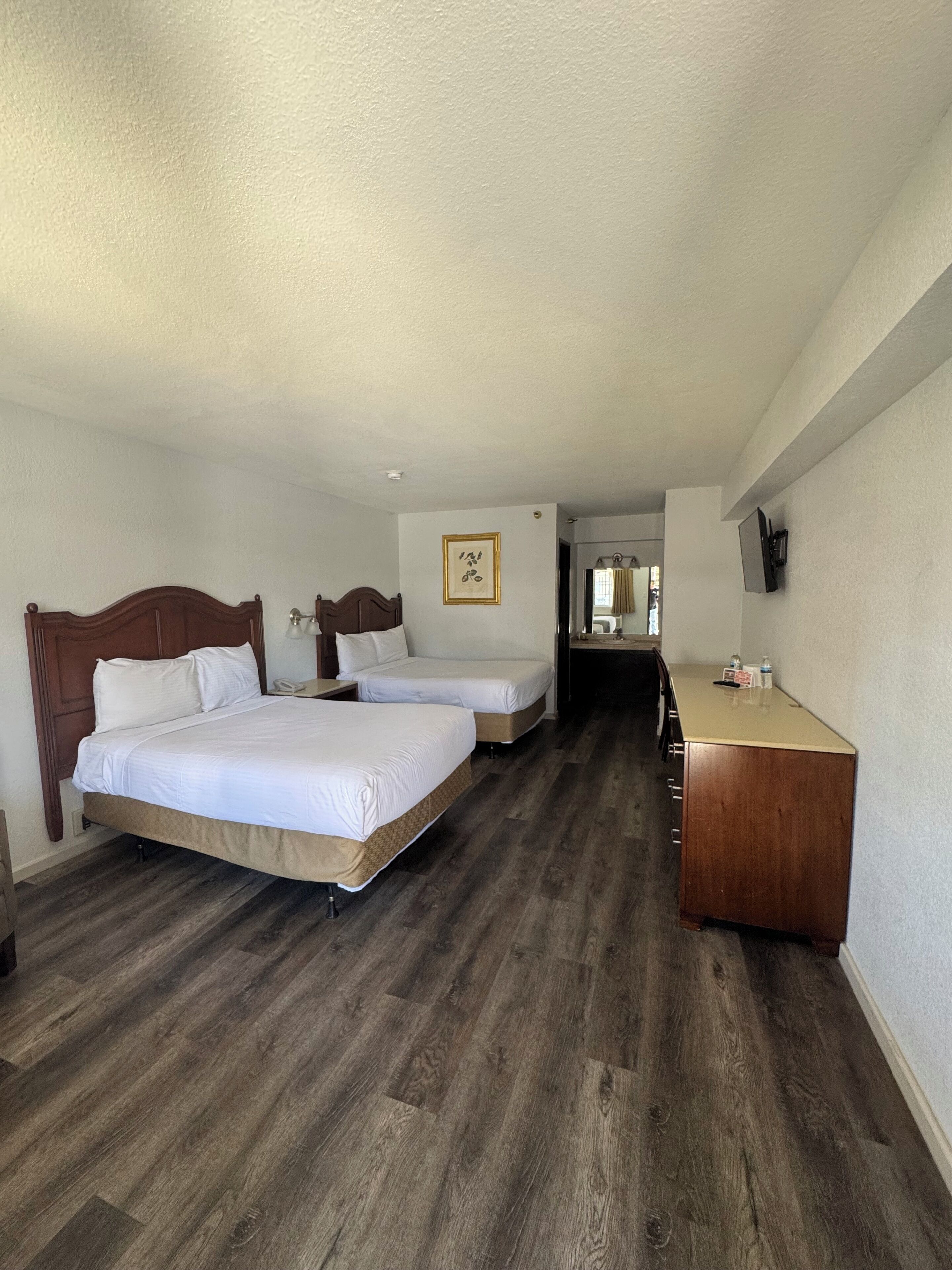Ein Hotelzimmer mit zwei Betten, einem Holzschrank, einem Schreibtisch und einem gerahmten Bild an der Wand.