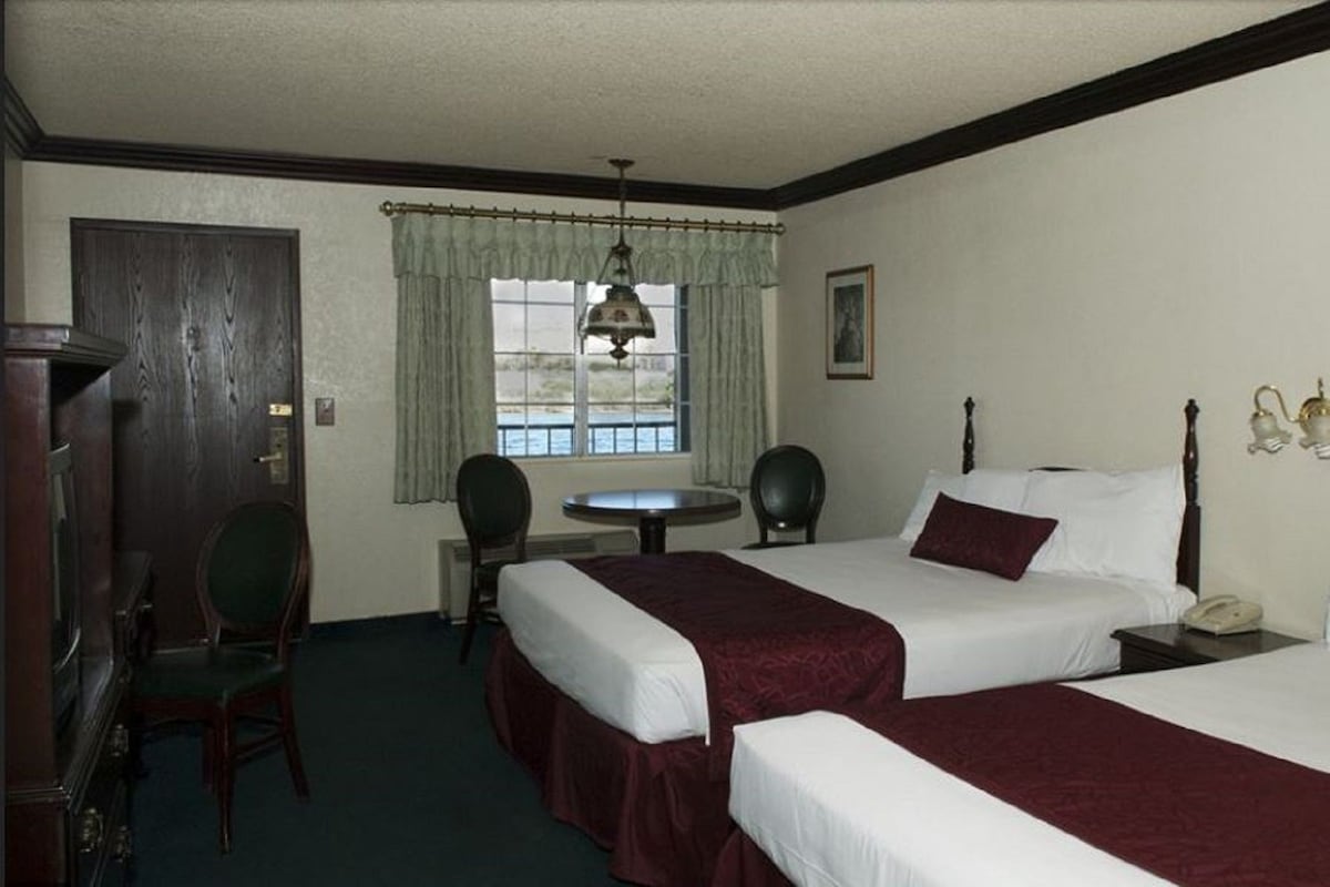 Habitación de hotel con dos camas, un escritorio, una silla, una ventana con cortinas y un teléfono.