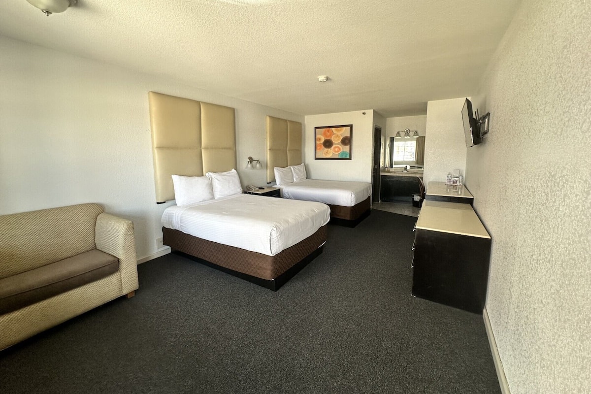 A hotel room with two beds, a sofa, a desk, a mirror, and a painting on the wall.