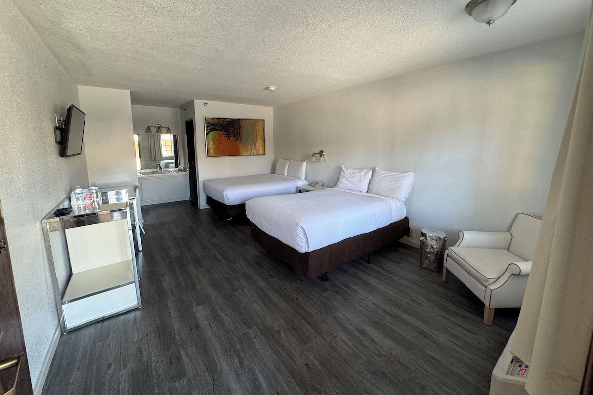 A hotel room with two beds, a desk, a chair, and a painting on the wall.